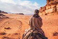 Young woman riding camel in desert. It\'s quite cold so she is wearing traditional Bedouin coat - bisht - and head scarf, Royalty Free Stock Photo