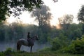Young woman riding a horse on a beautiful landscape. Clear lake at morning fog. Royalty Free Stock Photo