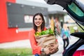 Young woman riding shopping cart full of food on the outdoor parking. Young woman in car park, loading shopping into boot of car. Royalty Free Stock Photo