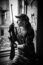 A young woman with a rifle in uniform at the window looking at the street. Female sniper in camouflage and cap. Black