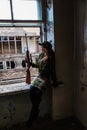 A young woman with a rifle in uniform at the window looking at the street. The woman sniper in a green suit and cap Royalty Free Stock Photo