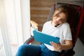 Young woman in room during quarantine. Businesswoman in chair talking on phone and look at tablet with smile. Hold