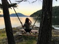 A young woman on a rope swing along the shore admiring the beautiful ocean view during sundown on an island