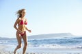 Young Woman Running Along Sandy Beach On Holiday Wearing Bikini Royalty Free Stock Photo