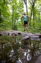 Young woman running forest trail past a stream with reflection in water