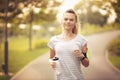 Young woman running in park and listening to music with headphones - Beautiful blonde and fit girl jogging alone outdoor in early