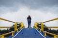 A young woman runs up a hill on a pedestrian bridge over a canal, a blue asphalt road, a yellow guardrail Royalty Free Stock Photo