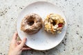 Young woman`s hand holding a plate with two tasty glazed donuts with chocolate, nuts and red cherry