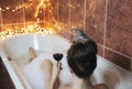 Young woman`s hand holding wine glass in bathtub, drinking red wine and lying in bathtub with bubble foam, top view, relaxtion an