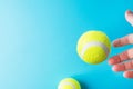 Young woman`s hand catching flying levitating in air yellow tennis balls on light blue background. Active lifestyle