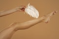 Young Woman`s Hand Touhing Her leg With White Feather On Beige Background. Beautiful Body Care Concepts Royalty Free Stock Photo