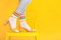 Legs of young woman in socks and sandals standing on chair against color background Royalty Free Stock Photo