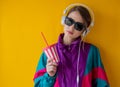 Young woman in 90s style clothes with cup and headphones