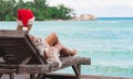 Young woman in santa claus hat sitting in chaise lounge on tropical sea beach Royalty Free Stock Photo