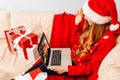 young woman in Santa Claus hat  using laptop  meets Christmas New Year via video call with family  sitting on sofa at home with Royalty Free Stock Photo