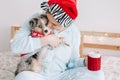 Young woman in Santa hat hugging kissing cute puppy dog pet at home. Pet owner celebrating Christmas holiday alone. Holiday Royalty Free Stock Photo