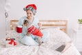 Young woman in Santa hat playing with cute puppy dog pet at home. Pet owner celebrating Christmas holiday alone. Distant remote Royalty Free Stock Photo