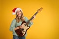 Young woman in Santa hat playing electric guitar on yellow background. Christmas music Royalty Free Stock Photo
