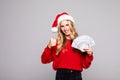 young woman in santa helper hat with thumbs up and holding dollar money banknotes isolated over grey background Royalty Free Stock Photo