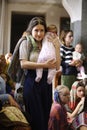 Young woman in a sari and baby on hands walking in a corridor of the Krishna tempe, people praying