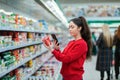 A young woman scans the QR code on a package of yogurt. In the background, a supermarket with visitors in a blur. The concept of Royalty Free Stock Photo