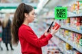 A young woman scans the QR code on a package of yogurt. A picture with a code is displayed above the product. Side view. The Royalty Free Stock Photo