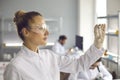 Young woman scientist looks at a test tube with white substance.
