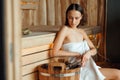 Young woman scoops up water from a wooden bucket in a sauna. Royalty Free Stock Photo