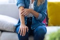 Young woman scratching her arm while sitting on the sofa at home Royalty Free Stock Photo