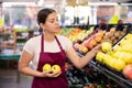 Young woman seller lays out apples in supermarket