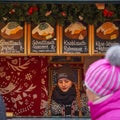 A young woman seller stands behind the counter in Christmas fair kiosk, selling baked potatoes in Vienna, Austria