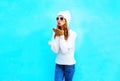 Young woman sends an air kiss in knitted sweater, hat on a blue Royalty Free Stock Photo