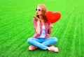 Young woman sends an air kiss with red balloon in the shape of a heart