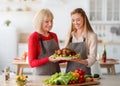 Young woman with senior mother holding dish with traditional turkey, cooking Christmas or Thanksgiving dinner in kitchen Royalty Free Stock Photo