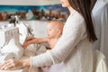 A young woman sews in the kitchen and holds a small child. Mom teaches her little son to sew on a sewing machine. Self Royalty Free Stock Photo