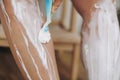 Young woman shaving legs with plastic razor closeup and depilation cream in home bathroom with green plants. Skin care. Hand Royalty Free Stock Photo