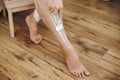 Young woman shaving legs with plastic razor and depilation cream in home bathroom with green plants. Skin care. Hand holding Royalty Free Stock Photo