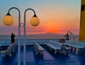 Young woman on a ship, taking photographs of the sunset, while the sun is behind distant island mountains, Royalty Free Stock Photo