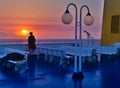 Young woman on a ship, taking photographs of the sunset, while the sun is behind distant island mountains, Royalty Free Stock Photo