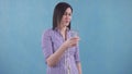Young woman with bewilderment drinks water from a glass standing on a blue background