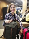 Young woman in shirt waiting for her transfer, with her backpack and luggage near her, looking into camera, smiling, blurred Royalty Free Stock Photo