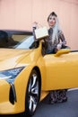 Young woman with shopping bag near the yellow super car, outdoors