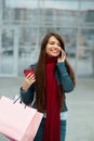 Young woman with shopping bags walking out from shop and talking on the phone. Woman with coffee. Consumerism, Royalty Free Stock Photo