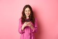 Young woman shopping, chatting on mobile phone, smiling while reading smartphone screen, standing against pink Royalty Free Stock Photo