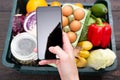 Young woman shopping groceries on online supermarket with her mobile phone.Box of grocery food and from store on background