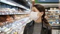 Young woman shopping in grocery store for food while wearing mask and preventing spread of coronavirus virus germs by wearing face