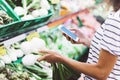 Young woman shopping healthy food in supermarket blur background. Female hands buy onion products and using smart phone in store Royalty Free Stock Photo