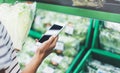 Young woman shopping healthy food in supermarket blur background. Female hands buy products cabagge using smart phone in store Royalty Free Stock Photo