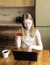 A young woman is shopping online from home. A girl with blonde hair holds a bank card in her hand and looks at the Royalty Free Stock Photo