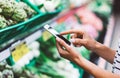 Young woman shopping purchase healthy food in supermarket blur background. Close up view girl buy products using smartphone in sto Royalty Free Stock Photo